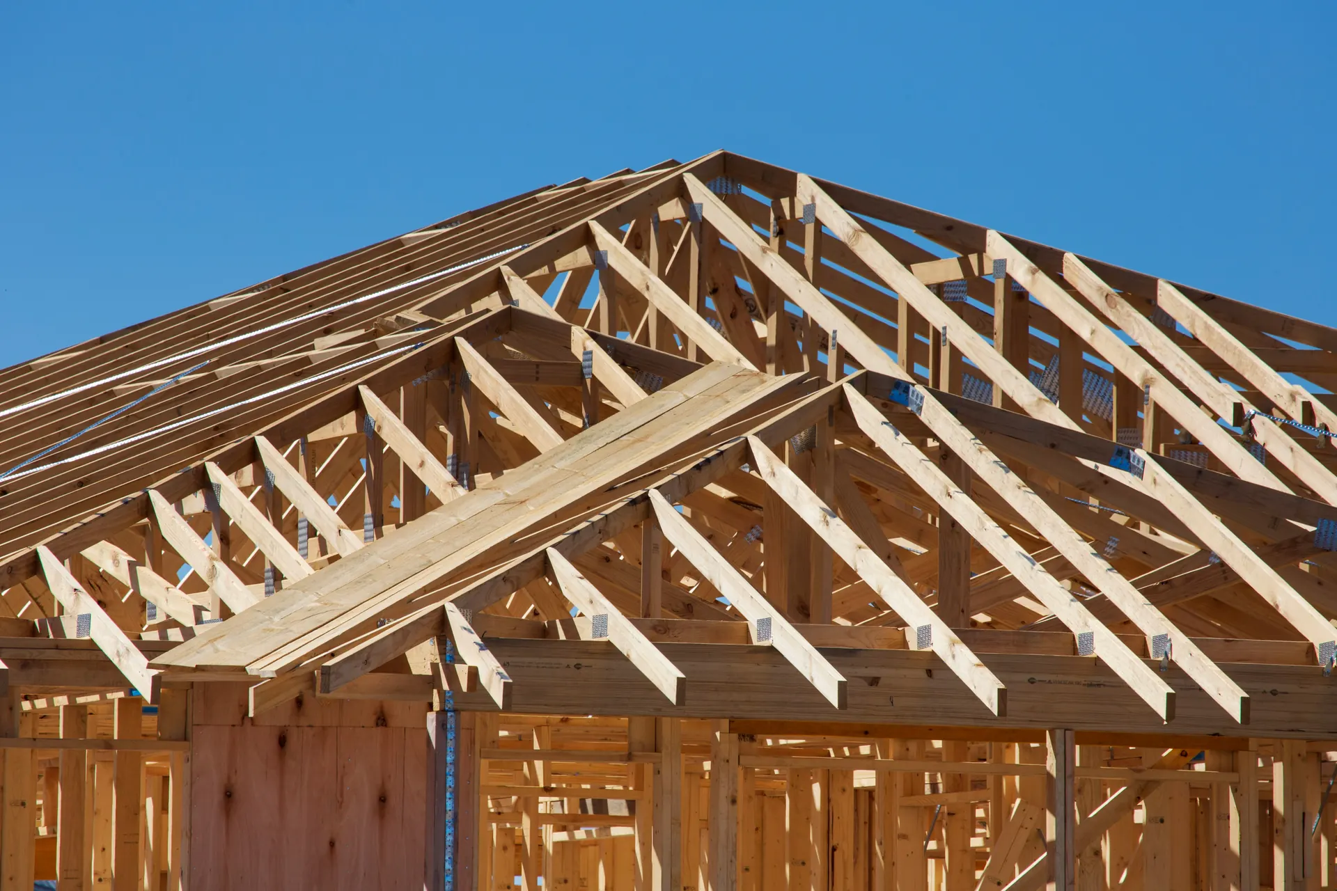Timber roof trusses on a house under construction against a blue sky
